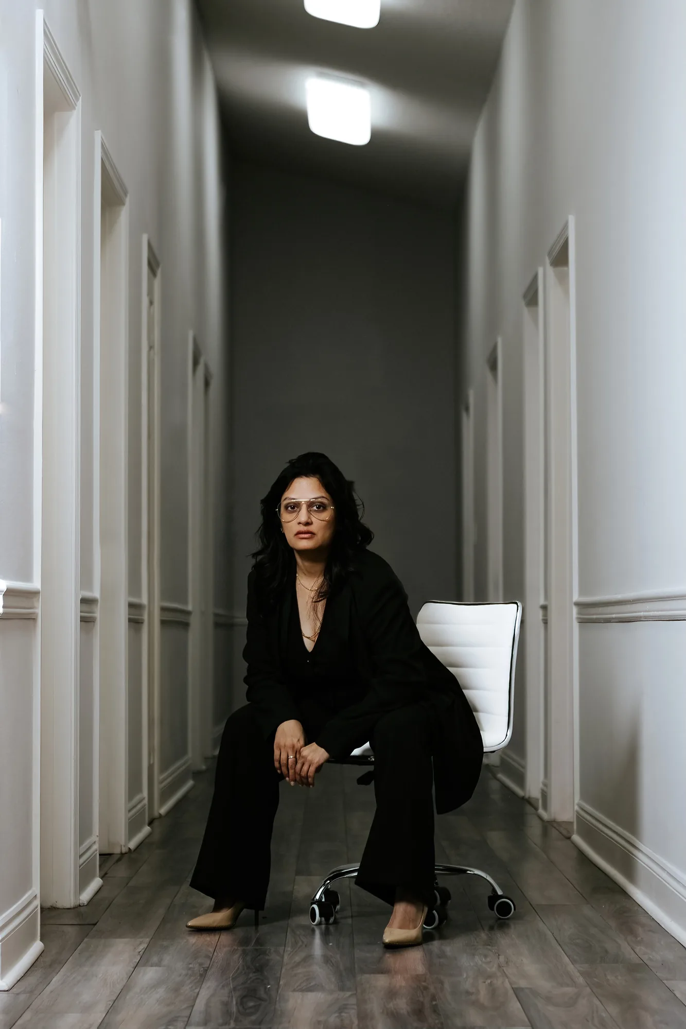 Dr. V seated in clinic hallway — clinical authority and precision